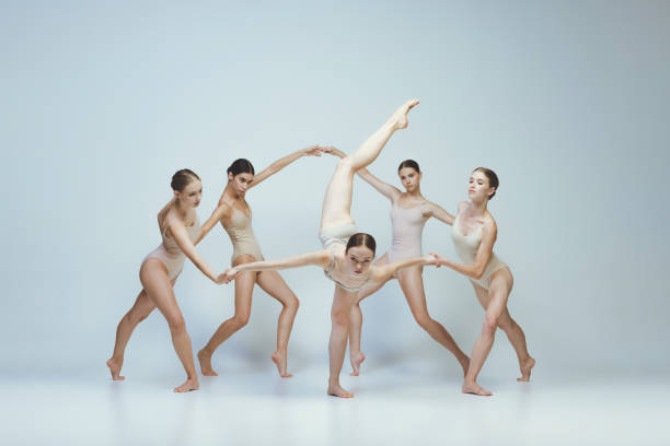 Group of young girls, ballet dancers performing, posing isolated over grey studio background. Holding hands. Concept of art, beauty, aspiration, creativity, classic dance style, elegance